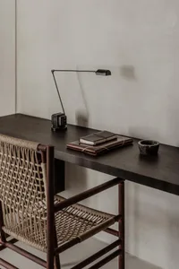A modern desk setup with a wooden desk, a woven leather chair, and a metal desk lamp.