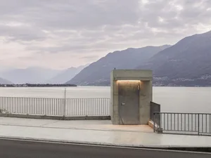 Concrete and glass minimalist entryway with illuminated door against a mountainous backdrop