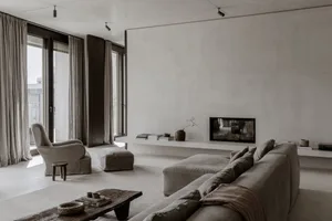 A modern minimalist living room featuring a concrete fireplace and furniture, with large windows and a neutral color palette.