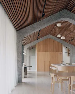 Modern interior space with wooden slat ceiling and walls, concrete structural elements, and minimalist furniture.