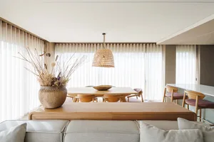 Minimalist-designed living and dining area with wooden tables and chairs, and a large vase with dried flowers.