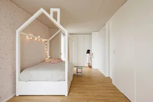 Modern children's bedroom with a house-shaped frame bed, wood flooring, and soft textiles.