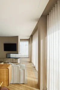 A modern minimalist living room featuring wooden flooring, cream fabric seating, and linen curtains.