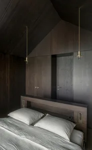 A serene minimalist bedroom with dark wood-paneled walls, white bedding, and brass pendant lights.