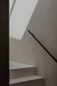 A minimalist staircase with a concrete wall and a black handrail.
