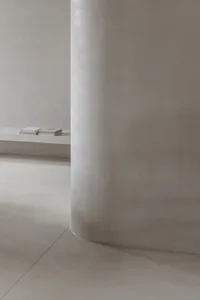 Minimalist room with a concrete floor and wall, featuring simple furniture and a floating shelf.