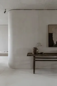 A simple, minimalist living room console table adorned with a vase of dried flowers and a bowl, against a smooth, white wall 