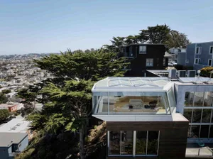A modern residential building with glass walls and wooden elements, featuring a glass roof and a living room with a couch.