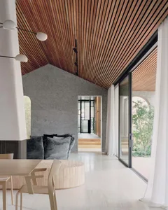 Modern living room with wooden ceiling, concrete walls, and large glass doors.