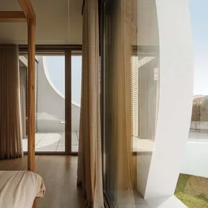 A minimalist residential bedroom featuring glass walls, wooden elements, and beige fabric curtains.