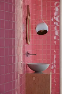 Modern minimalist bathroom with pink ceramic tiles, wooden basin, and concrete flooring.