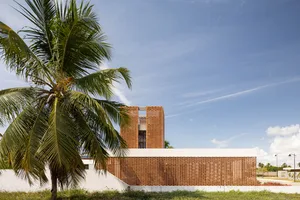 A modern brick building with a palm tree in the foreground against a blue sky.