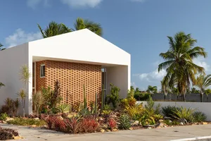 Modern building exterior with white overhang and red brick wall surrounded by colorful plants