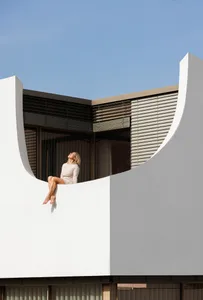 A woman sitting on a curved white architectural element against a clear blue sky.