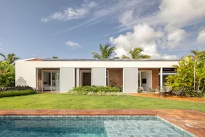 A modern house with a brick and concrete exterior, featuring a pool and outdoor seating area surrounded by greenery.