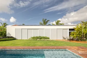 White modern house with solar panels on the roof surrounded by greenery and a swimming pool.
