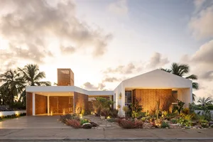 A modern residential home featuring brick walls and a sandy driveway at sunset.