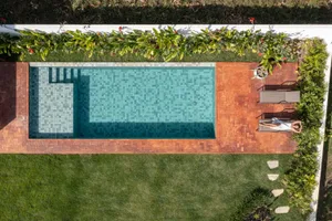 Aerial view of a modern poolside area featuring composite tiles and concrete, with a person sunbathing on a lounge chair.