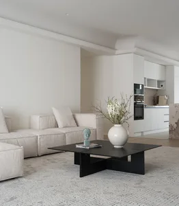 A minimalist living room with neutral-colored cotton fabrics and a black coffee table holding a white vase with flowers.