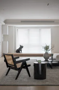 A minimalist living room featuring a black armchair with woven cane backrest, a black coffee table, and a large window with w
