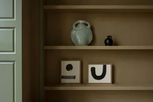 Modern interior design featuring a ceramic vase and abstract paintings on shelves.