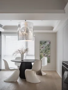 Modern minimalist dining room featuring a black round table with white chairs and a glass chandelier.