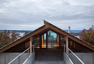 A modern architectural structure featuring a wooden roofline with large windows overlooking a scenic landscape.