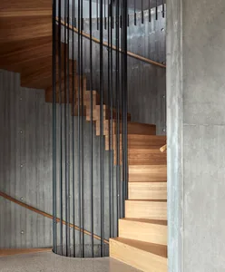 Circular staircase with wooden steps and black metal railings, surrounded by concrete walls.