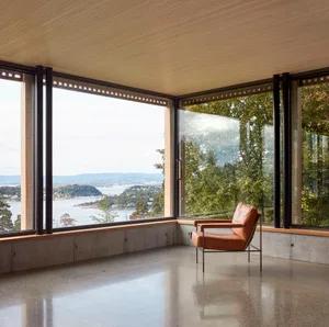 Modern living space featuring floor-to-ceiling windows, concrete flooring, and a comfortable chair with a view of the water a