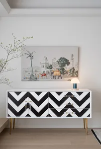 A modern living room with a white and black zigzag-patterned dresser, a table lamp, and a framed painting depicting a desert 