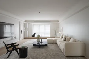A minimalist living room with a wooden floor, a beige sectional sofa, and a black side table with a green cup and saucer.