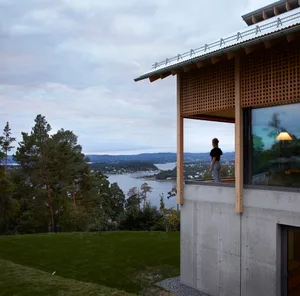 Modern minimalist residential exterior with concrete and wood features overlooking a scenic body of water.