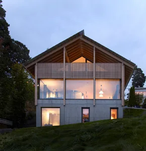 A modern residential house with concrete and wood exterior, featuring a large window and a wooden balcony.
