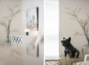 A modern living room featuring a plant with long branches in a vase, a table lamp, and a wall painting.