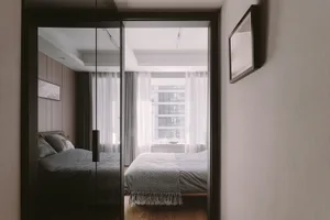 A minimalist bedroom featuring a bed with white curtains and a grey bedspread, set against a grey wall and hardwood floor.