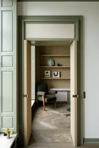 A minimalist office space with a wooden parquet floor, shelving, and a comfortable chair.