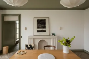 A modern residential dining room featuring minimalist design, with stone fireplace, wooden table, and abstract artwork on the