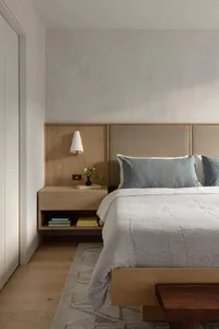 A minimalist bedroom featuring a wooden headboard and fabric blanket on a bed with books and a plant on a floating nightstand