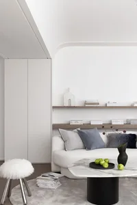 A modern, minimalist living room with a white sofa, wooden shelves, and a marble coffee table.