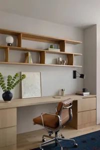 A modern office space featuring a wooden desk with shelves, a brown leather office chair, and various office supplies.