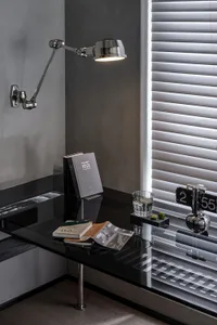 A modern interior desk featuring a glass surface, a sleek lamp, books, and a glass of water on top of it.