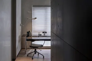 A modern office space with minimalist decor, including a glass desk, metal chair, and concrete walls.