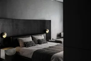 A minimalist bedroom with a dark wood headboard and light bedding, featuring modern sconce lighting and a sleek, low-profile 
