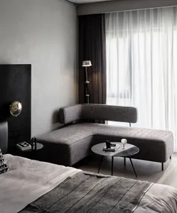 A modern minimalist bedroom featuring a textured fabric sofa, a large window with sheer curtains, and a floor lamp.