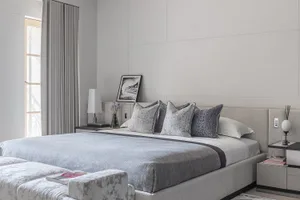Modern minimalistic bedroom featuring upholstered furniture, neutral color palette, and abstract artwork.