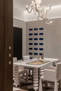 A modern dining room features a white-painted table and chairs with a decorative chandelier hanging above it.