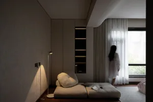 A minimalist bedroom with a textured wall, featuring a soft seating area with cushions and a small table.