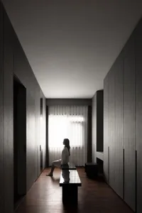 A minimalist interior space with wood elements, featuring a woman sitting on a bench by a window.