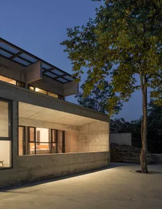 Modern residential exterior featuring a concrete facade at dusk, with interior lights illuminating through large glass window