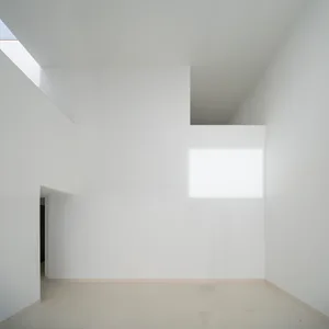 A minimalist white interior space with a high ceiling, light shining through a window, and a clean, uncluttered design.